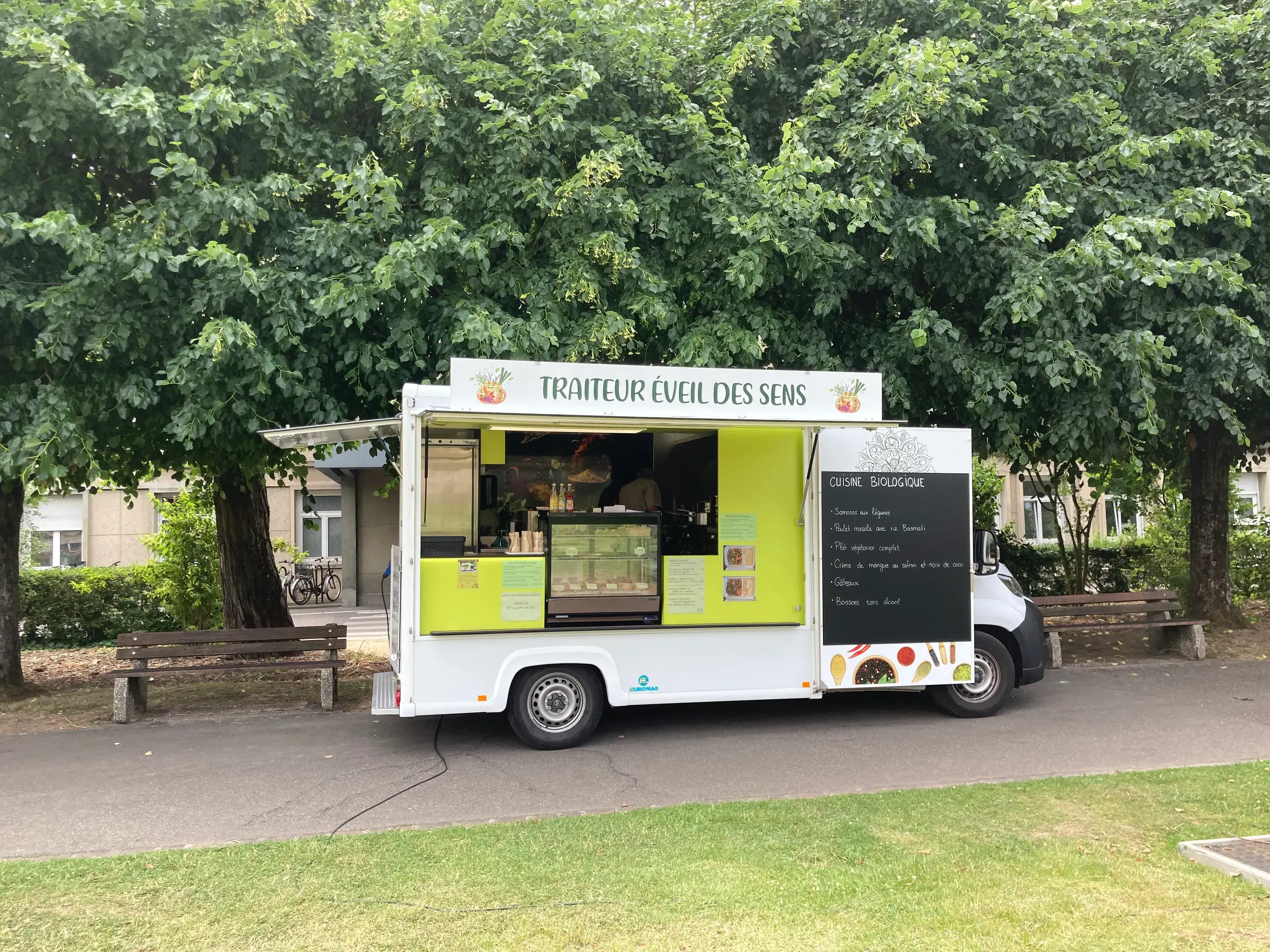 Le foodtruck Traiteur Éveil des Sens, volet vert anis ouvert et ardoise du jour, installé sous les arbres